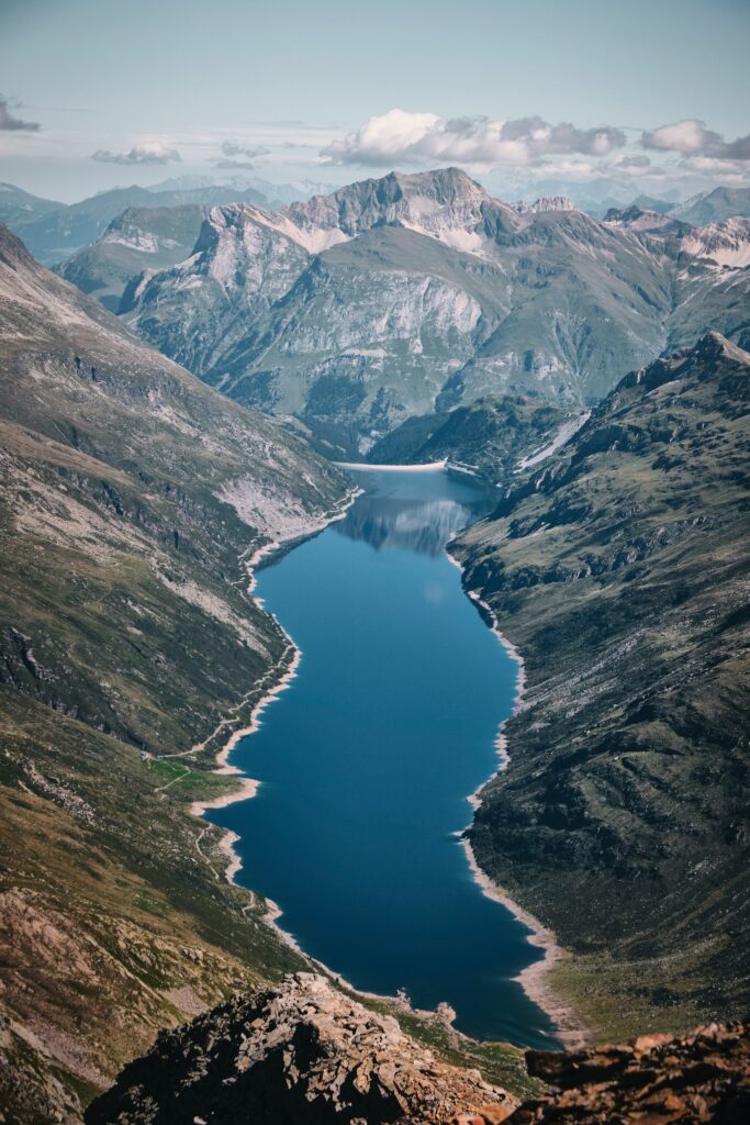 Aerial view of blue lake winding through rugged mountains with green slopes and rocky terrain Wallpaper