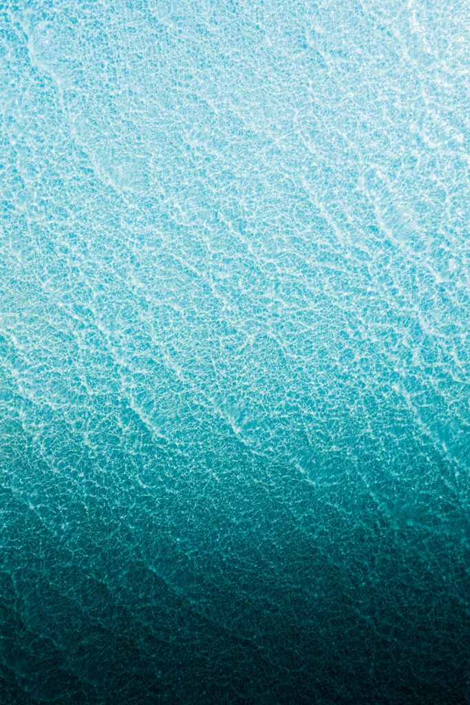 Aerial view of turquoise sea with gentle waves forming white patterns minimalist ocean wallpaper background