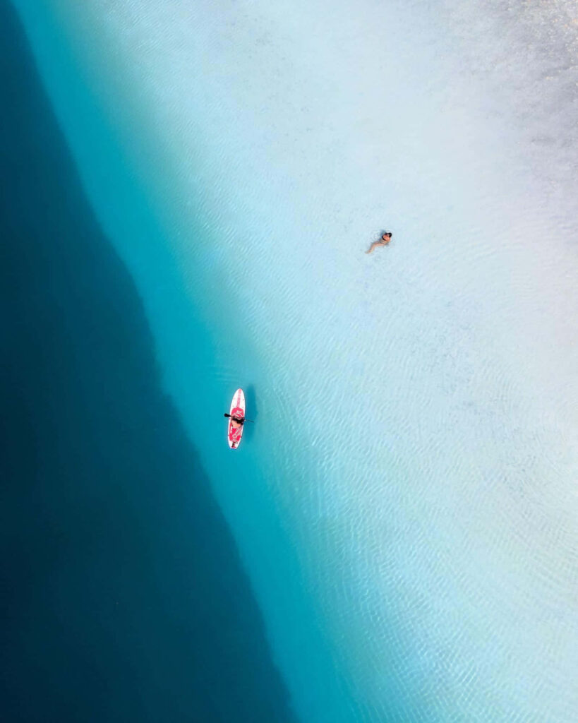 Stunning Aerial Ocean Wallpaper: Paddleboarder & Swimmer in Blue Waters