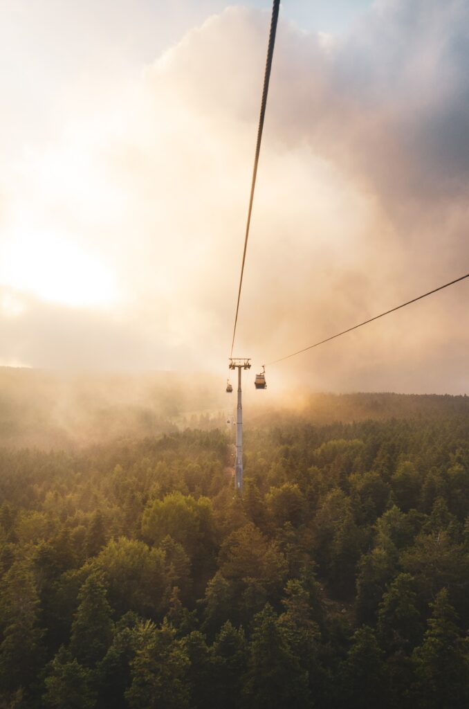 Aerial view of cable cars above misty forest with soft sunlight creating a peaceful atmosphere Wallpaper