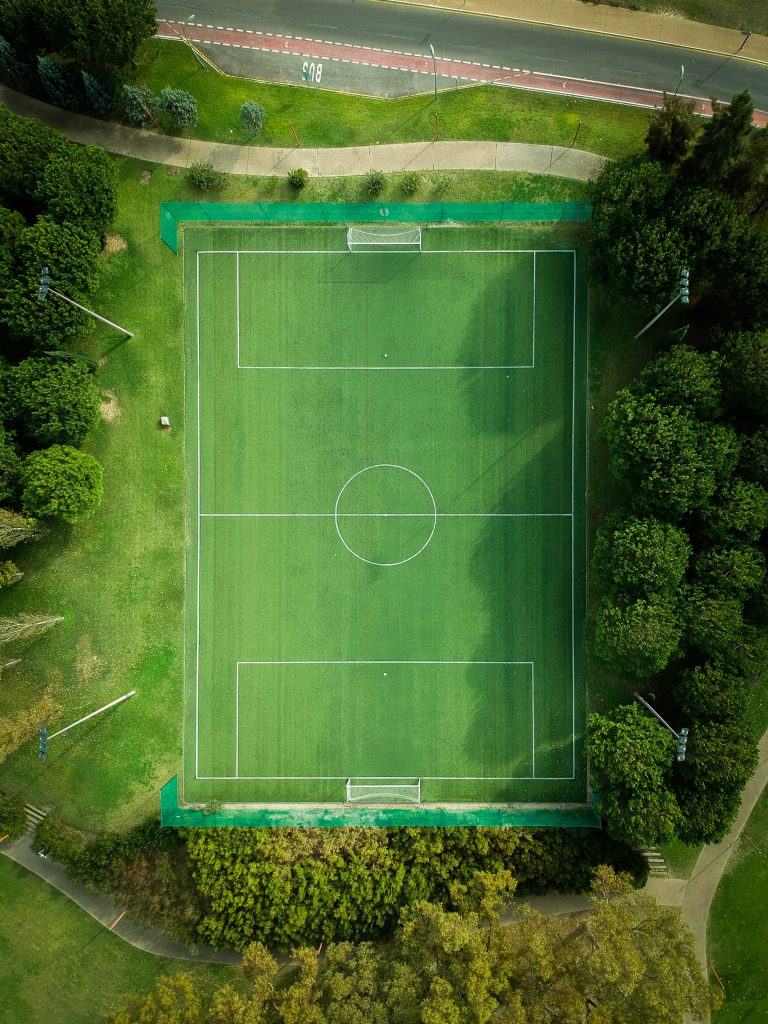 Aerial view of empty soccer field surrounded by trees with soft natural lighting sports wallpaper