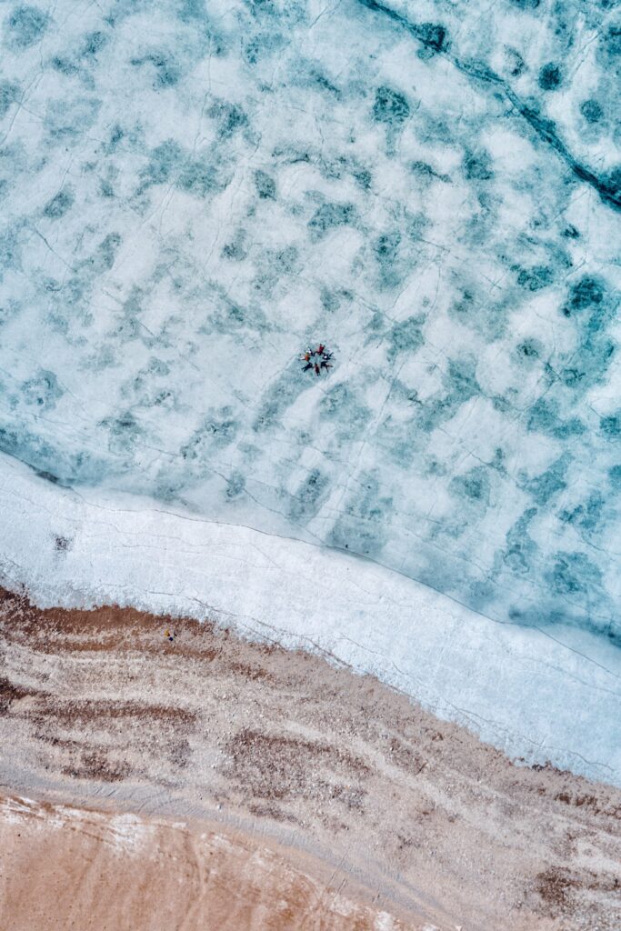 Aerial view of frozen blue white lake with people lying center rocky shore winter landscape wallpaper