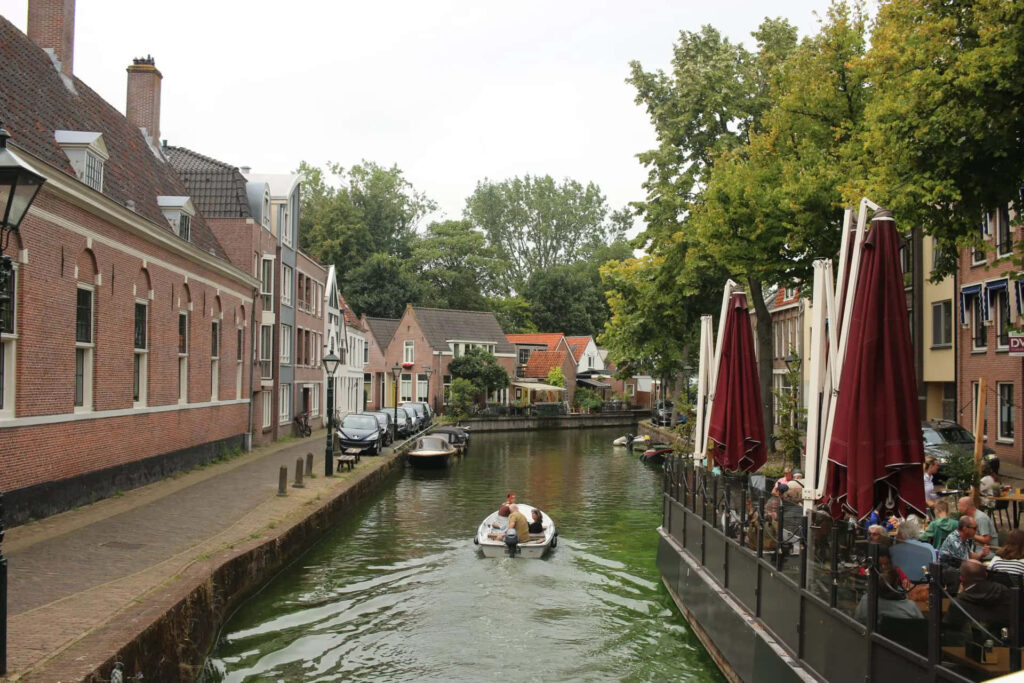 Serene Alkmaar canal with boat and lively outdoor riverside cafe background wallpaper