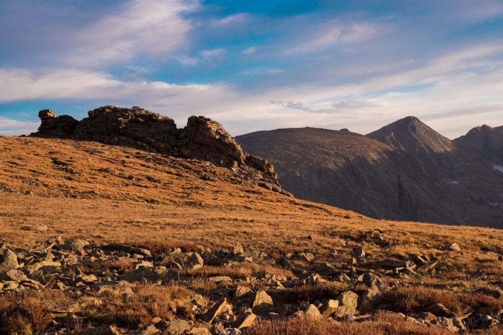 Serene alpine landscape with golden meadows rugged rocks and majestic mountain peaks under blue sky Wallpaper