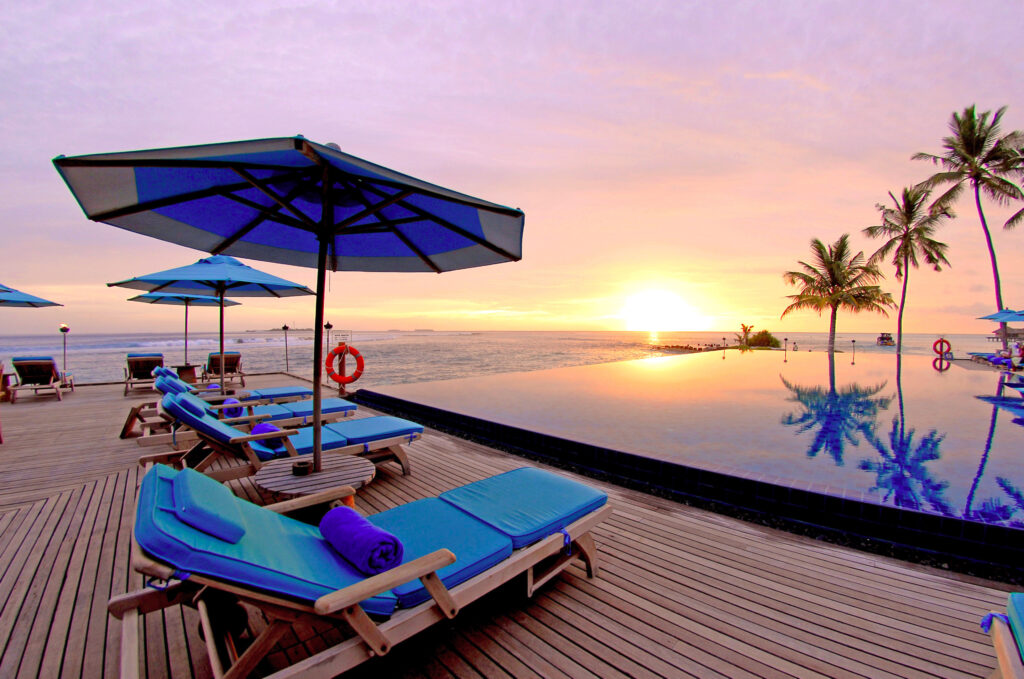 Sun loungers and umbrellas at Anantara Veli Resort Maldives infinity pool with sunset ocean view Wallpaper