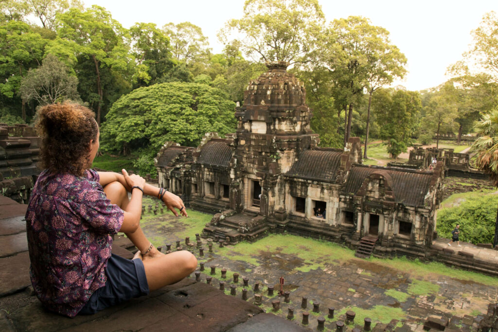Tourist atop Angkor Thom ruins overlooking historic temples surrounded by lush greenery Wallpaper
