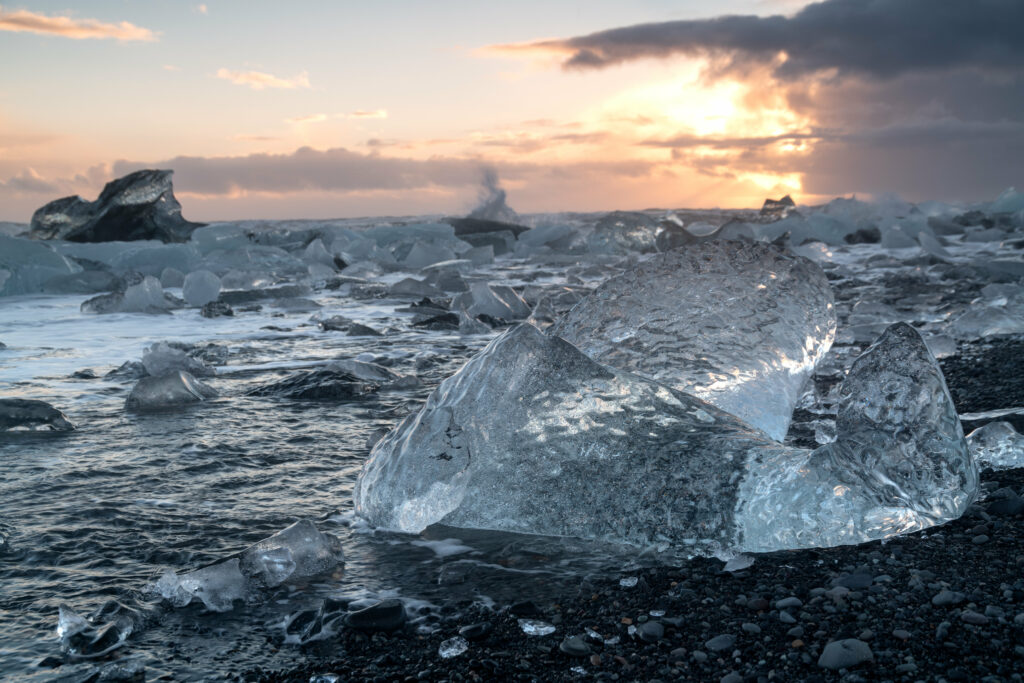 Crystal clear icebergs by rugged coastline with gentle waves and dramatic sunset arctic scene Wallpaper