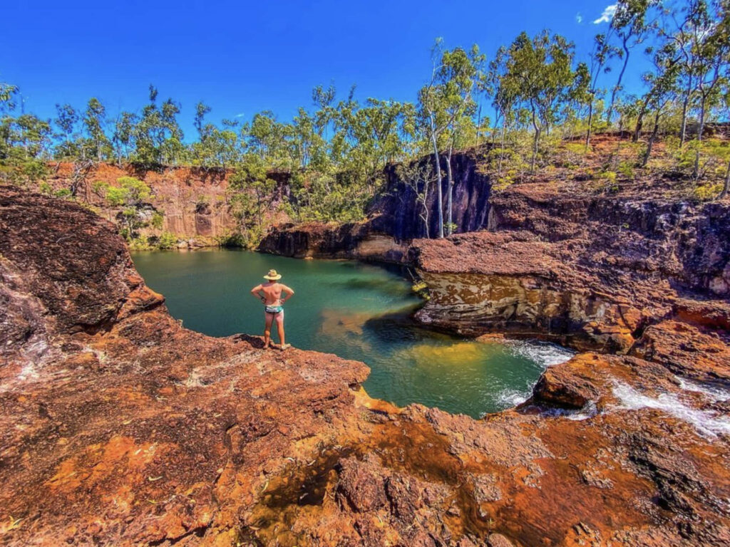 Adventurer by serene waterhole with red rocks and lush trees under clear blue sky Arnhem Land wallpaper