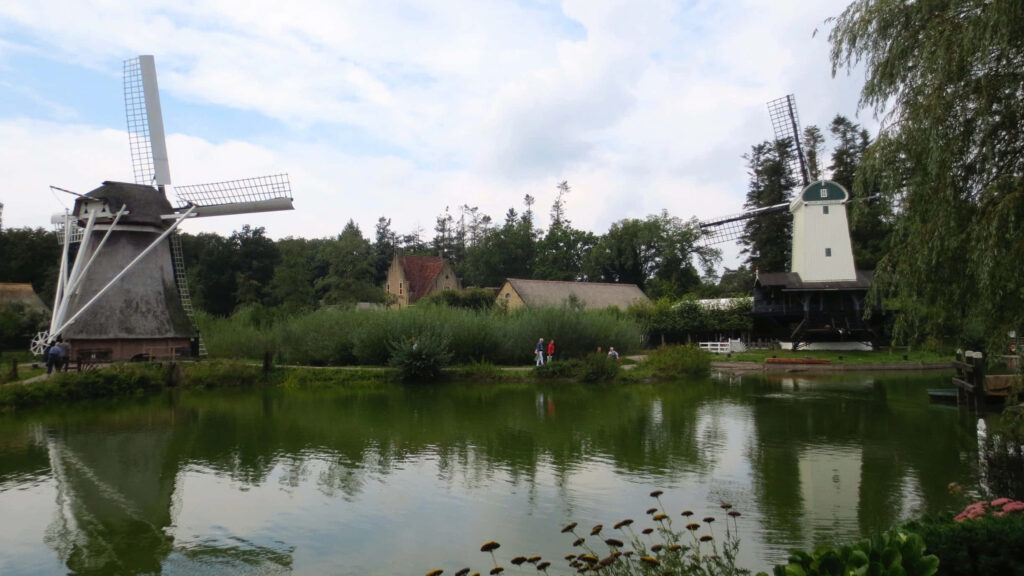 Historic windmills reflecting on calm pond surrounded by greenery at Arnhem Open Air Museum Wallpaper
