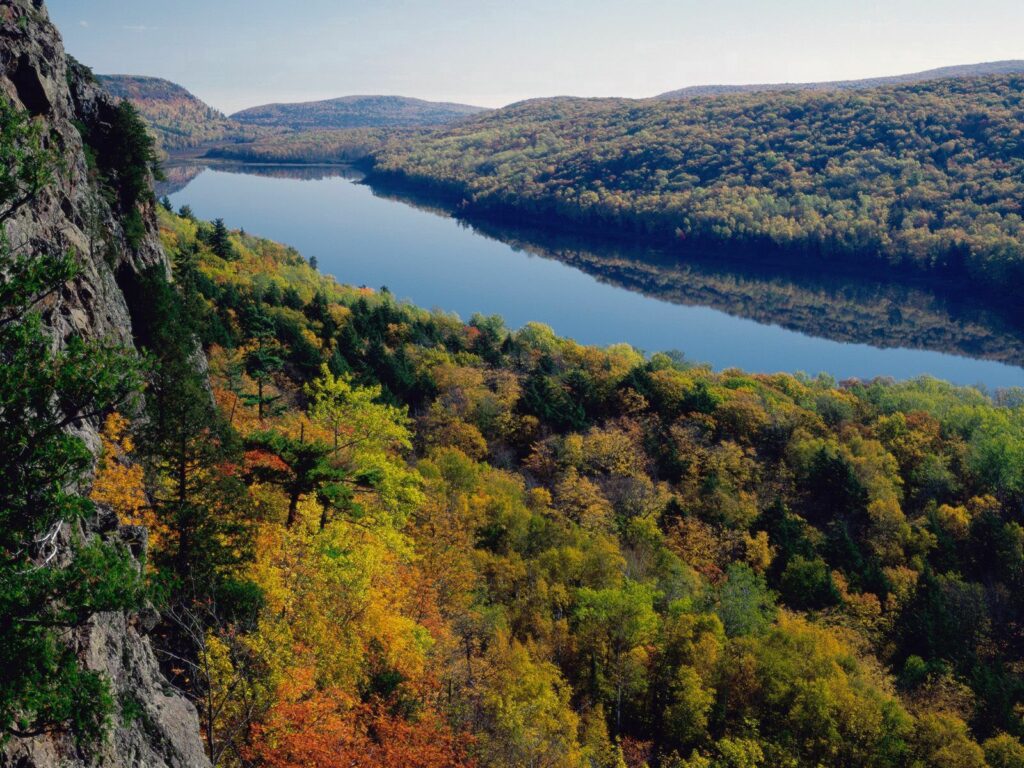 Aerial view of serene river winding through colorful autumn forest with lush hills wallpaper