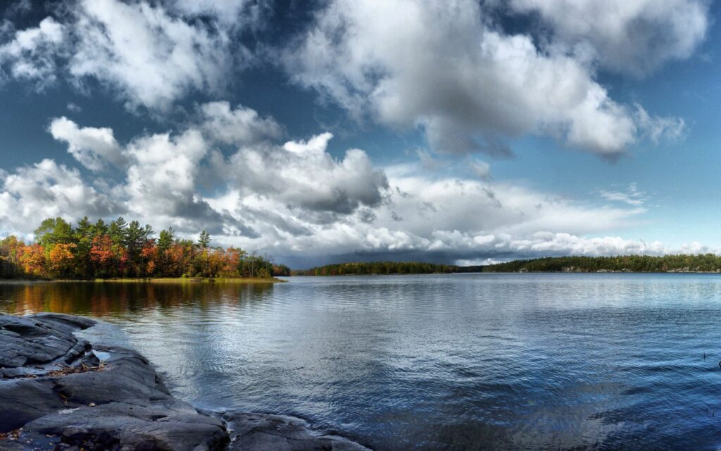 Calm lake reflecting dramatic autumn sky and colorful trees serene fall nature wallpaper background