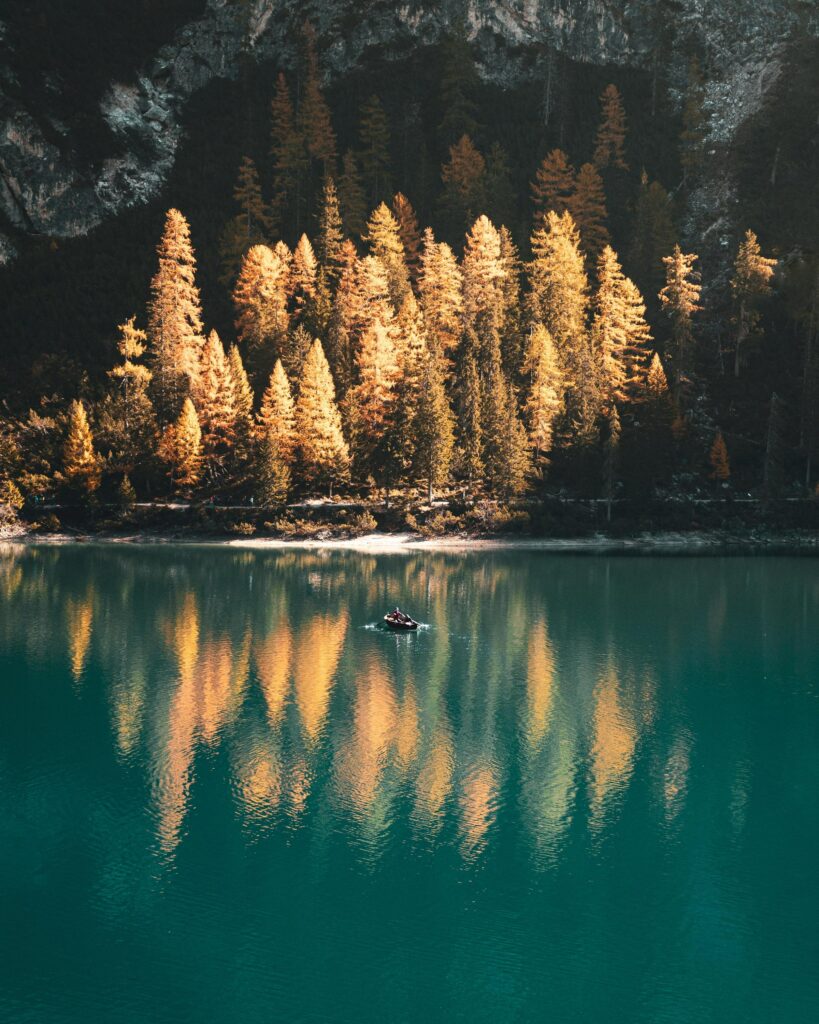 Serene autumn landscape with golden trees and boat on turquoise lake reflecting fall foliage Wallpaper