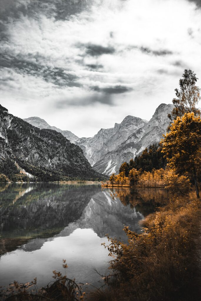 Serene mountain landscape with rugged peaks reflected in calm lake and golden autumn trees Wallpaper