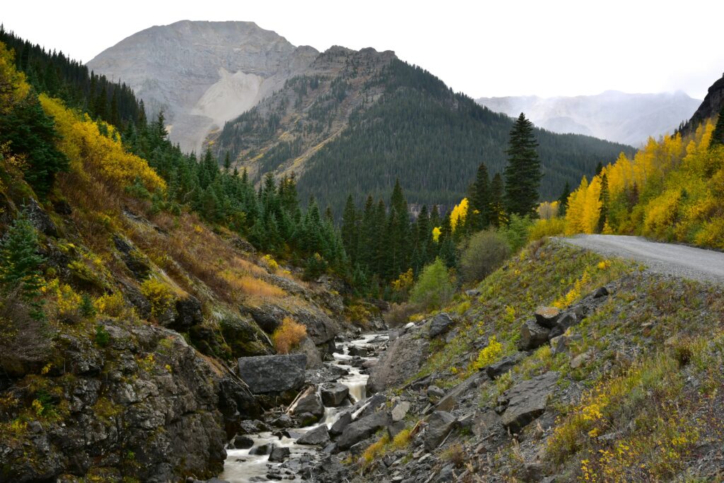 Serene river flowing through autumn forest with rugged rocks and distant majestic mountains background Wallpaper