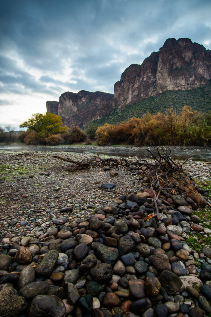 Serene autumn river landscape with smooth stones branches vibrant foliage and distant mountains Wallpaper