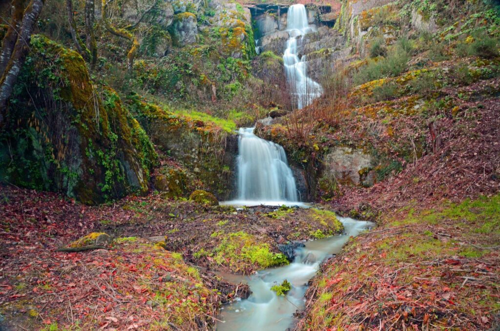 Serene autumn waterfall over mossy rocks with vibrant red orange green foliage mountain scene Wallpaper