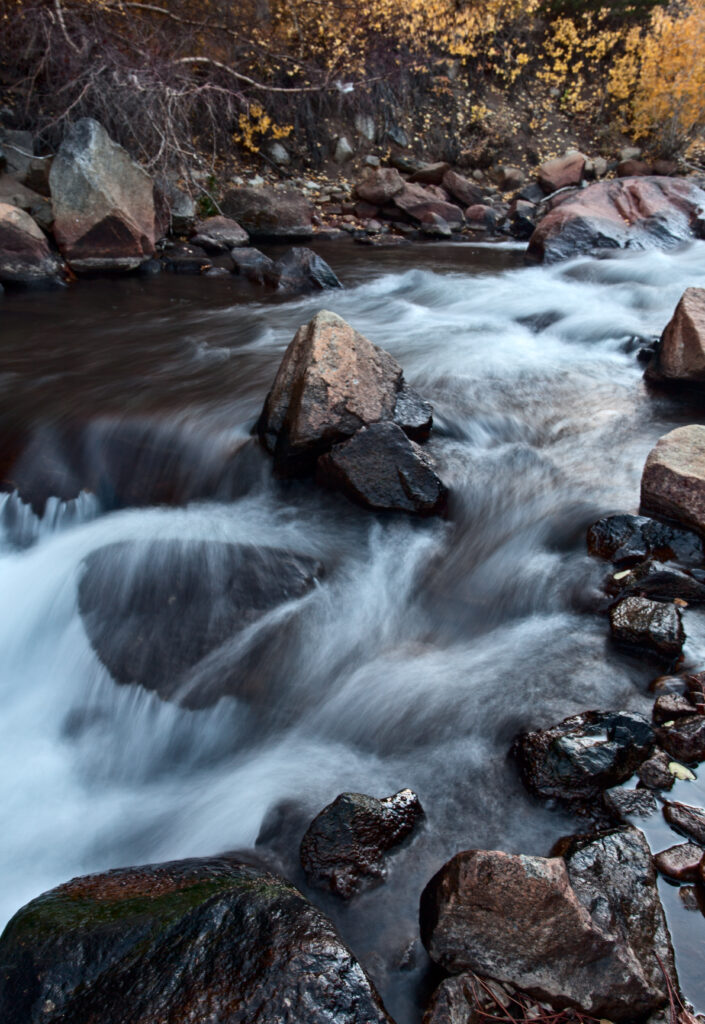 Silky waterfall over smooth river stones with autumn foliage in serene natural landscape wallpaper