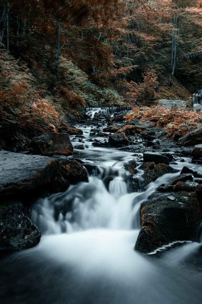 Serene waterfall over rocks with autumn forest and clear stream natural wallpaper background