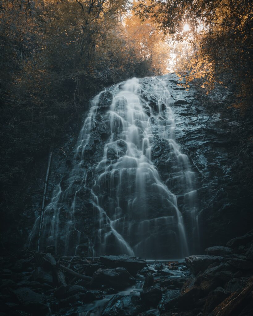 Serene waterfall over dark rocks with autumn trees and golden light peaceful nature scene wallpaper