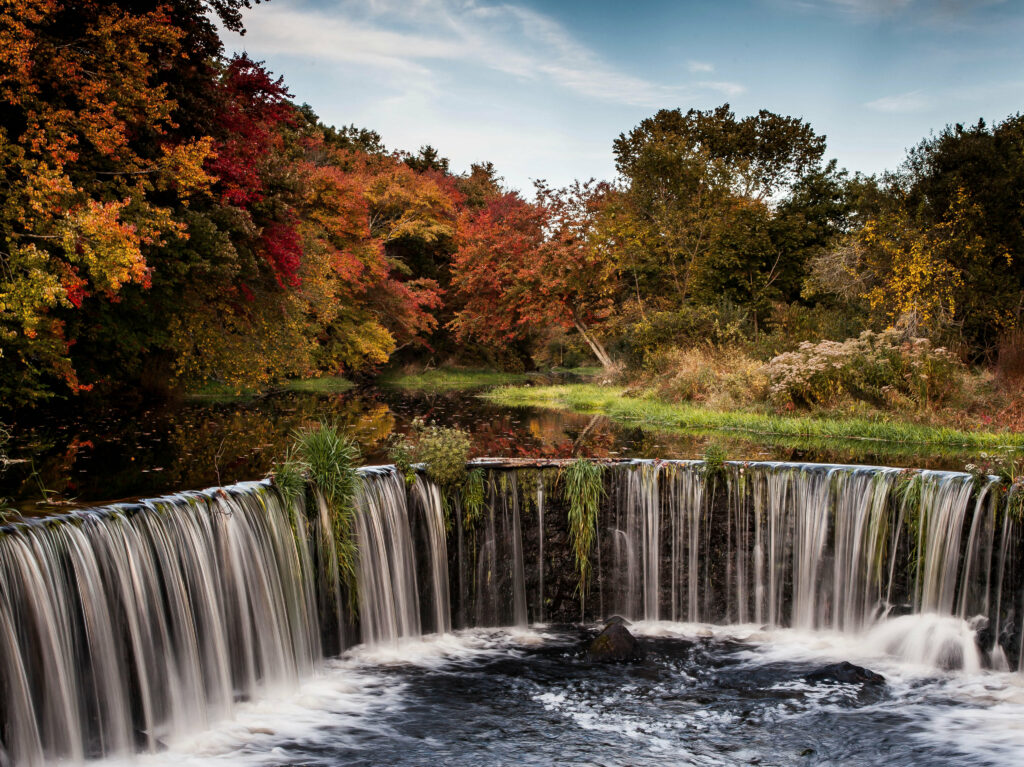 Autumn waterfall flowing into stream with vibrant orange gold and green trees peaceful nature Wallpaper