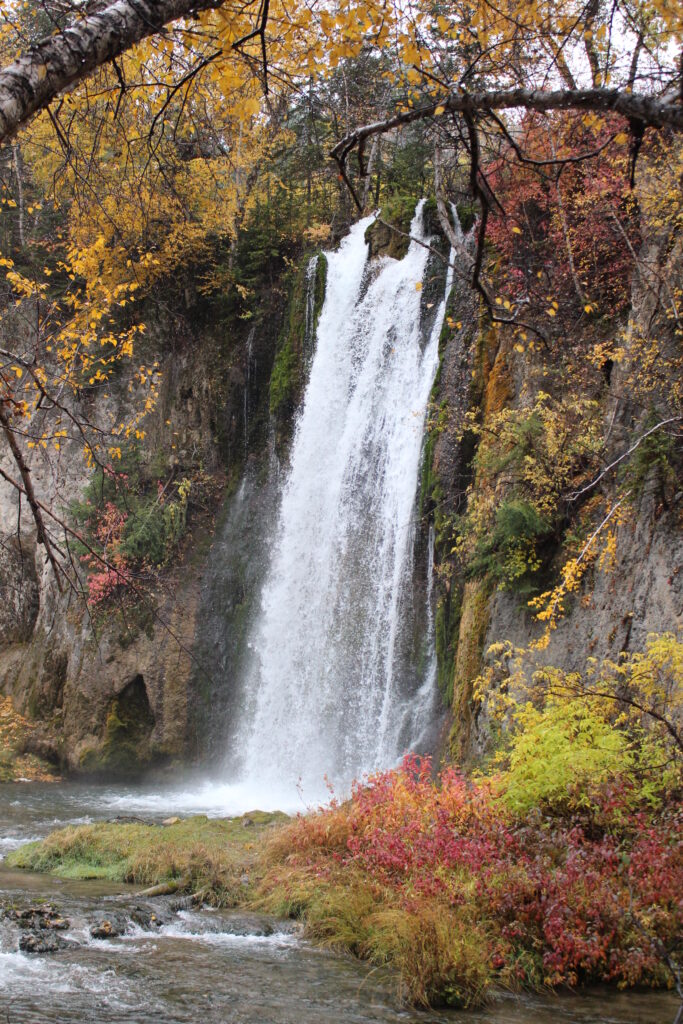 Serene waterfall flowing over rocks surrounded by vibrant autumn trees and colorful foliage Wallpaper