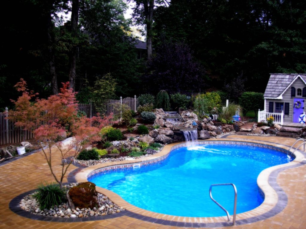 Serene backyard oasis with eight-shaped pool natural stone waterfall lush landscaping garden shed Wallpaper