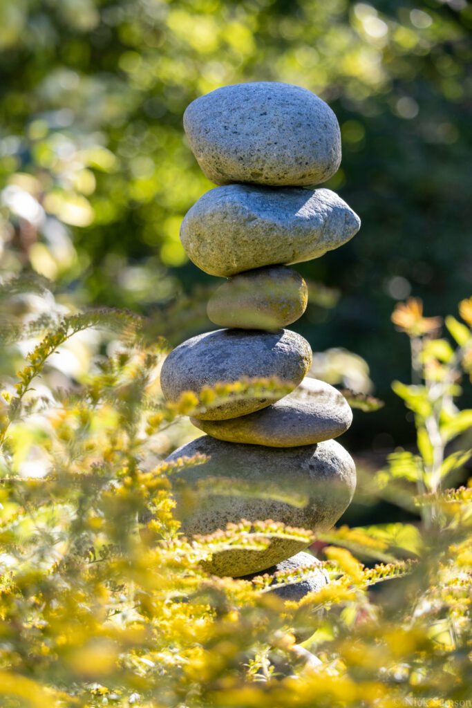 Stack of smooth stones balanced on green grass with golden foliage in a tranquil natural background Wallpaper