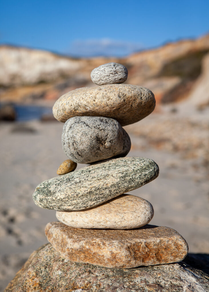 Serene wallpaper of smooth balanced stones on sandy beach with soft blue sky for calmness