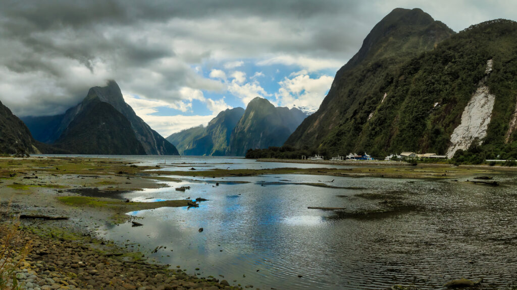 Serene bay with green mountains and dramatic clouds reflecting on calm water landscape wallpaper
