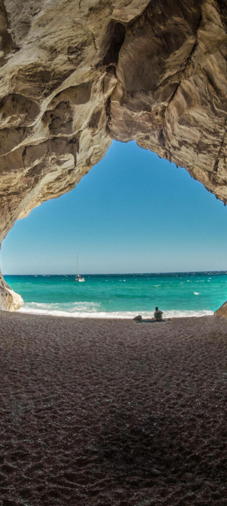 Serene Beach Cave View: Turquoise Ocean & Sailboat Wallpaper