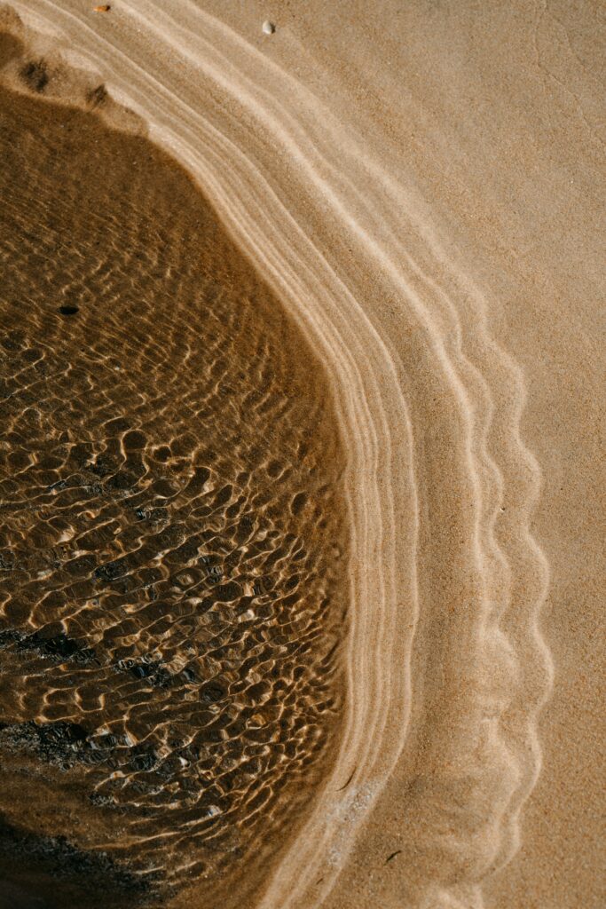 Tranquil beach wallpaper with golden sand and sunlight highlighting gentle water ripples