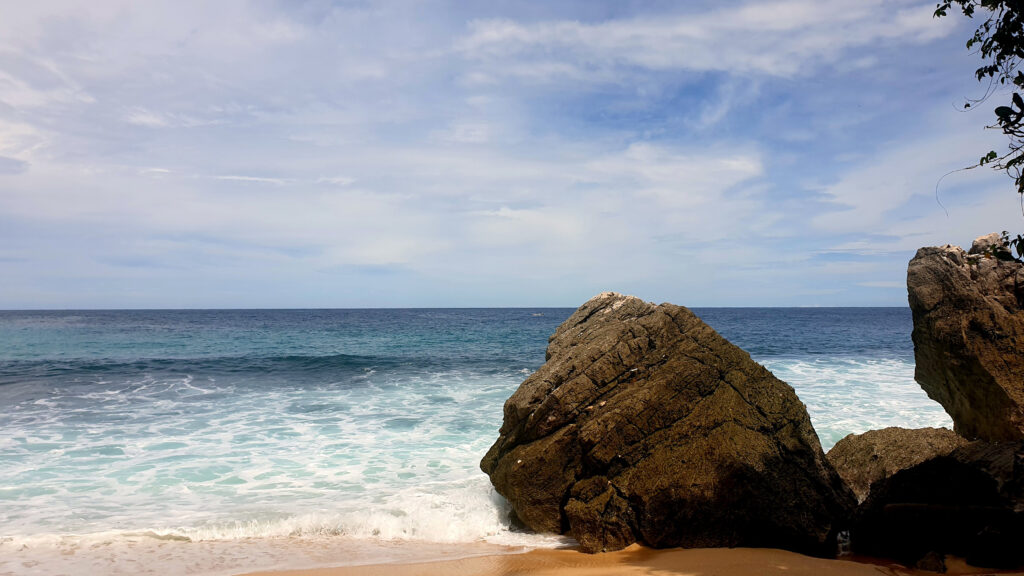 Serene beach wallpaper with soft sand powerful waves large textured rocks and calm blue sky