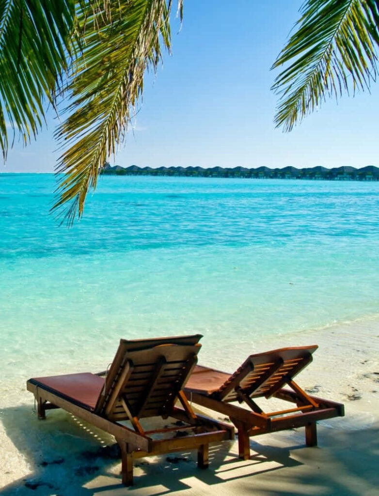 Tranquil Beach Scene with Wooden Chairs and Turquoise Waters Wallpaper