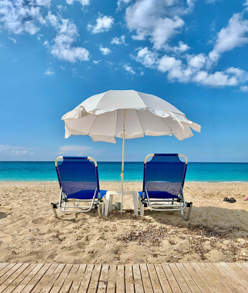 Relaxing Beach Scene: Blue Lounge Chairs & Umbrella Under Clear Skies Wallpaper