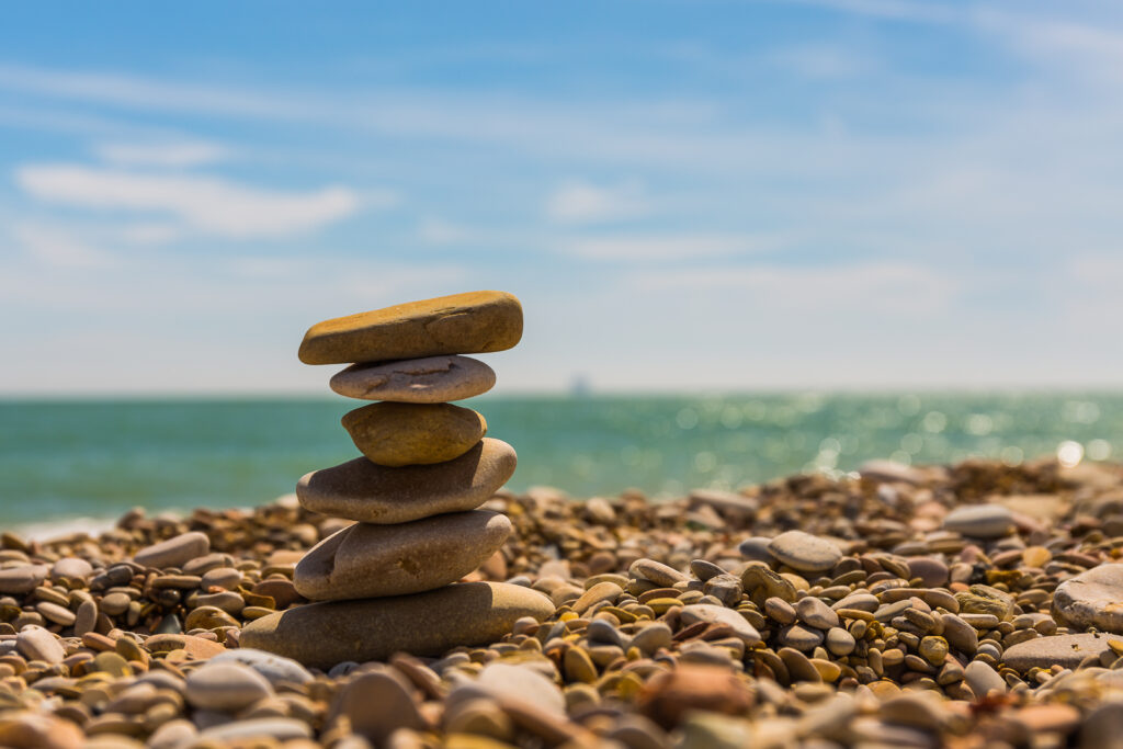 Serene beach scene with balanced smooth stones sunlit sea and blue sky calm wallpaper background