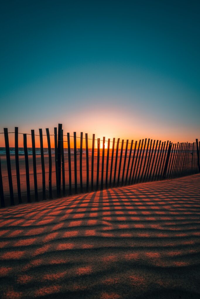 Serene beach sunset with golden light casting fence shadows on rippled sand vibrant sky Wallpaper