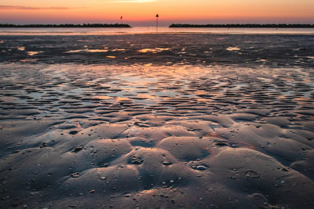 Serene beach sunset with rippling shallow water over textured sand warm orange pink hues Wallpaper