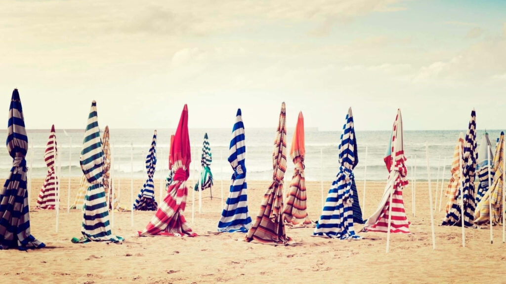 Colorful Striped Umbrellas on Serene Beach: A Picturesque Scene Wallpaper