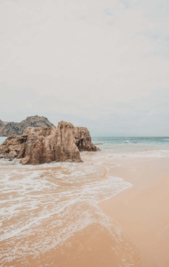 Tranquil Beach with Sandy Shores, Waves, and Coastal Rocks Wallpaper