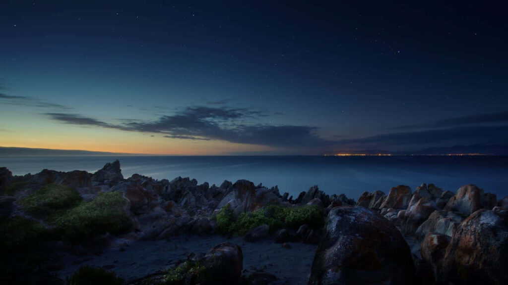 Serene Beach Wallpaper: Rugged Rocks & Starlit Ocean Background
