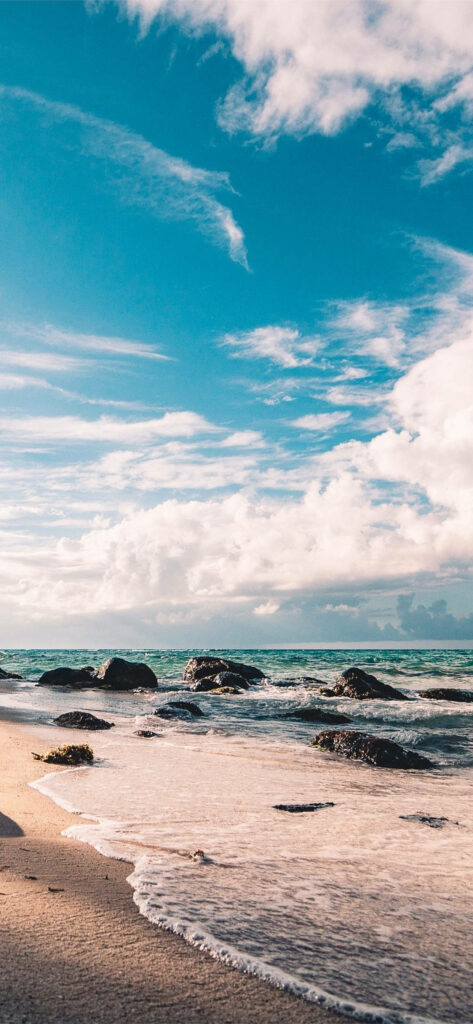 Serene Beach Scene: Tide, Smooth Rocks & Blue Sky Background Wallpaper