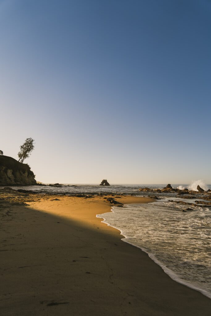 Serene beach wallpaper with gentle waves golden sand rugged rocks and clear blue sky background