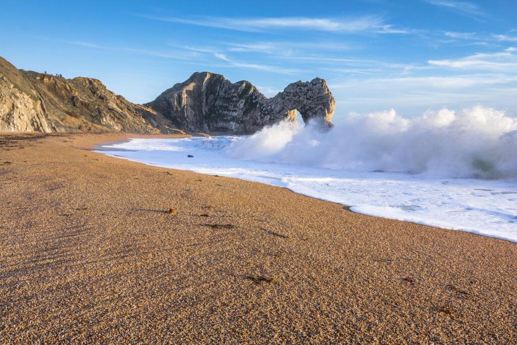 Serene beach wallpaper with golden sand crashing waves rugged rocks and clear blue sky background