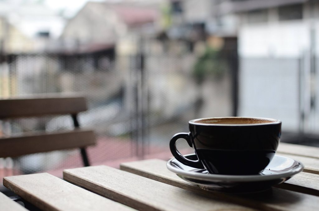 Black coffee cup on rustic wooden table with soft natural light and dreamy bokeh cafe background Wallpaper