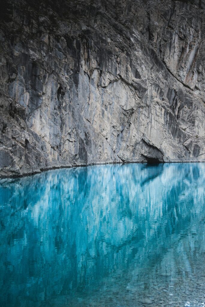 Serene blue lake reflecting towering rocky cliff and mountain with vibrant water and natural textures Wallpaper