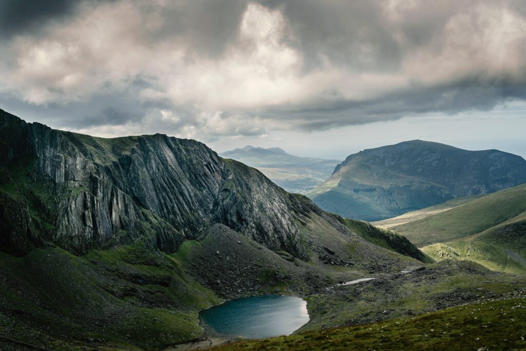 Tranquil blue lake surrounded by rugged mountains and dramatic hills under moody sky wallpaper