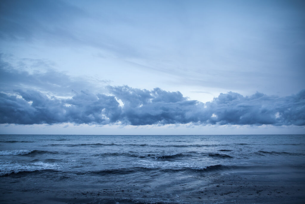 Calm blue sea with gentle waves and dramatic cloudy sky creating serene wallpaper background