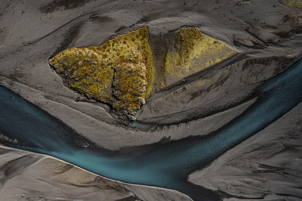 Aerial view of blue river winding around lush triangular island with green and yellow vegetation Wallpaper