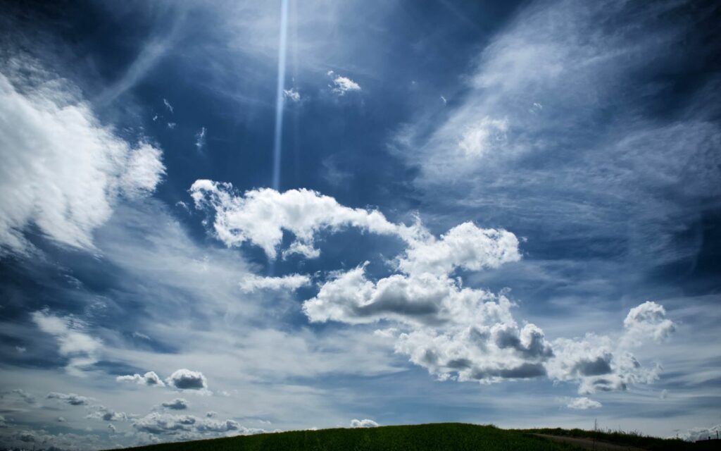 Vivid blue sky with soft clouds and sunlight over a peaceful green horizon wallpaper background