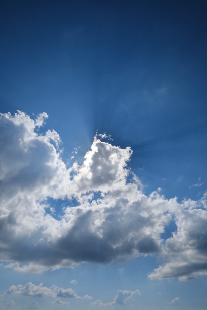 Serene blue sky with fluffy white clouds and sunlight rays creating a peaceful atmosphere Wallpaper